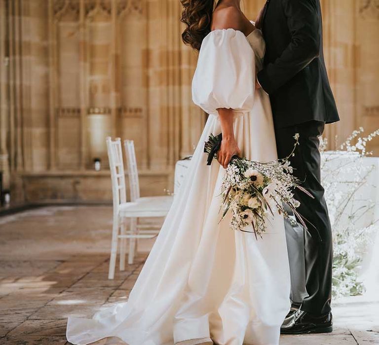 Bride in a full skirt wedding dress with detachable puff sleeve holding a white wedding bouquet with anemones 