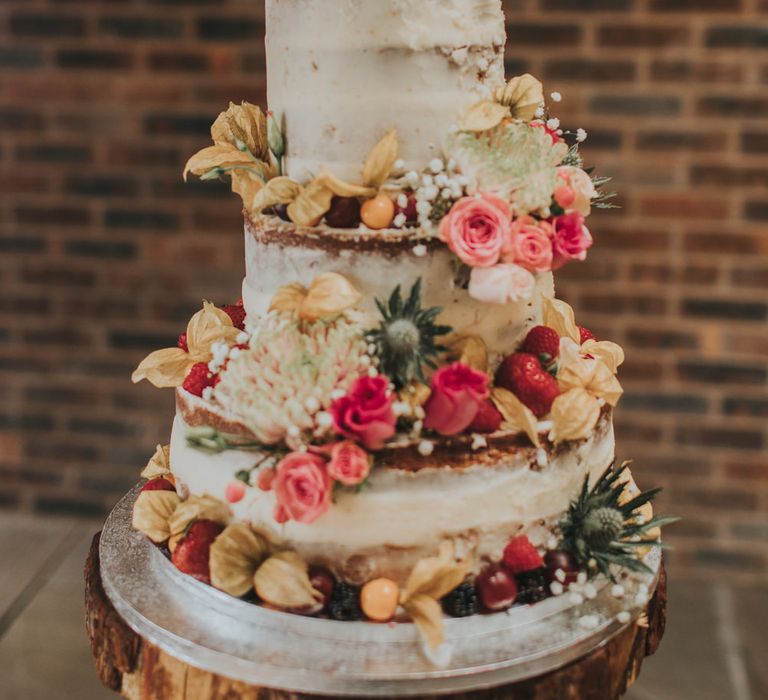 Semi naked wedding cake on a wooden tree slice with floral decor and personalised wooden laser-cut cake topper 