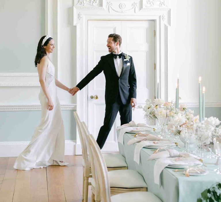 Groom in a tuxedo escorting his bride in a fitted wedding dress to their pale green wedding reception at Botley's Mansion