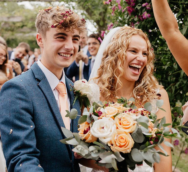 Bride & groom laugh and smile on their wedding day whilst confetti is thrown around them