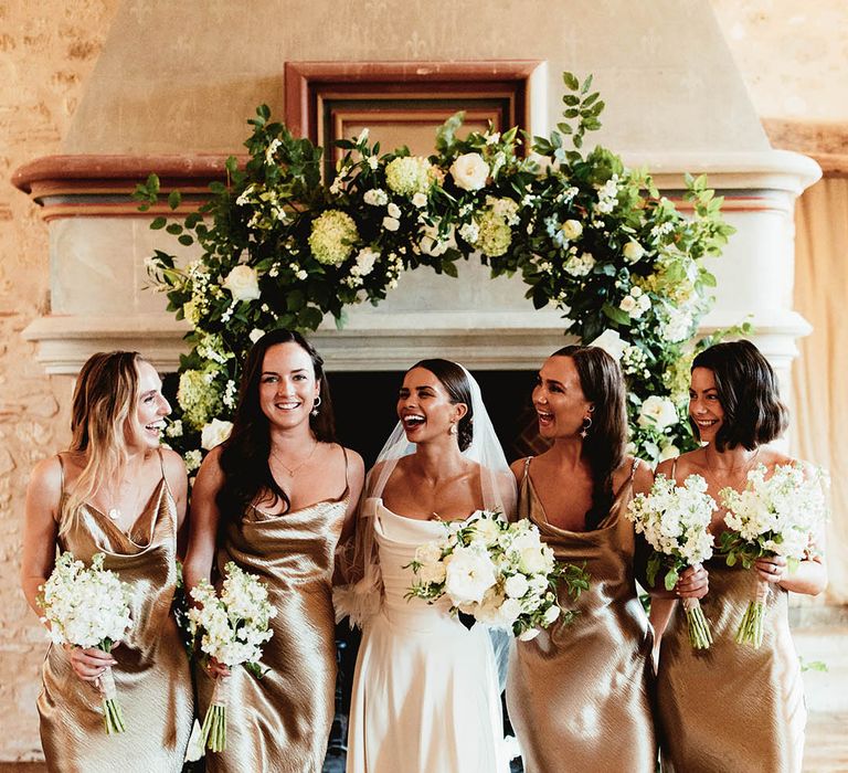 Bride stands with her bridesmaids who wear gold satin dresses with straps