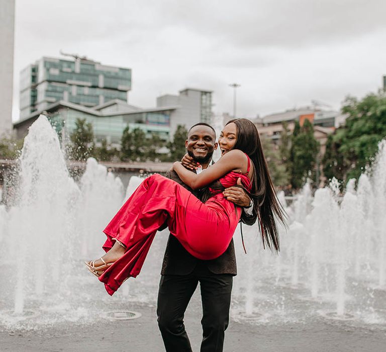 Groom lifts his bride who wears sleek red gown 