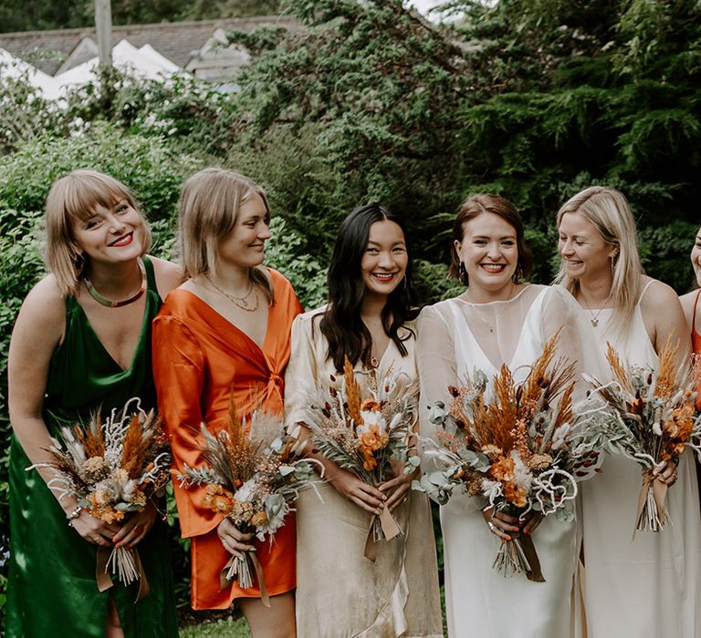 Bridal party photograph with bridesmaids in orange and green satin dresses holding dried orange flower bouquets 