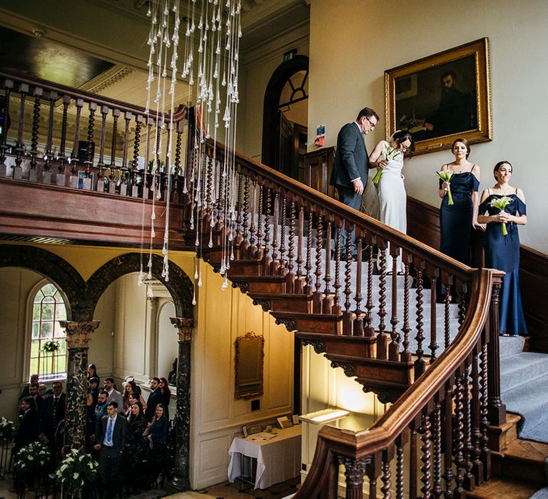 Bride walks down the stairs with her family on wedding day