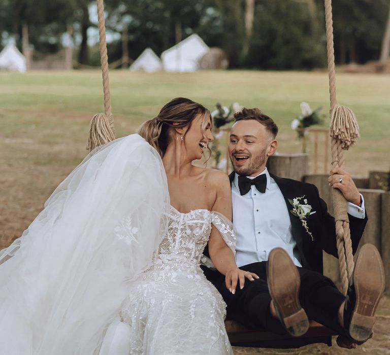 Bride sits with her groom on swing outdoors