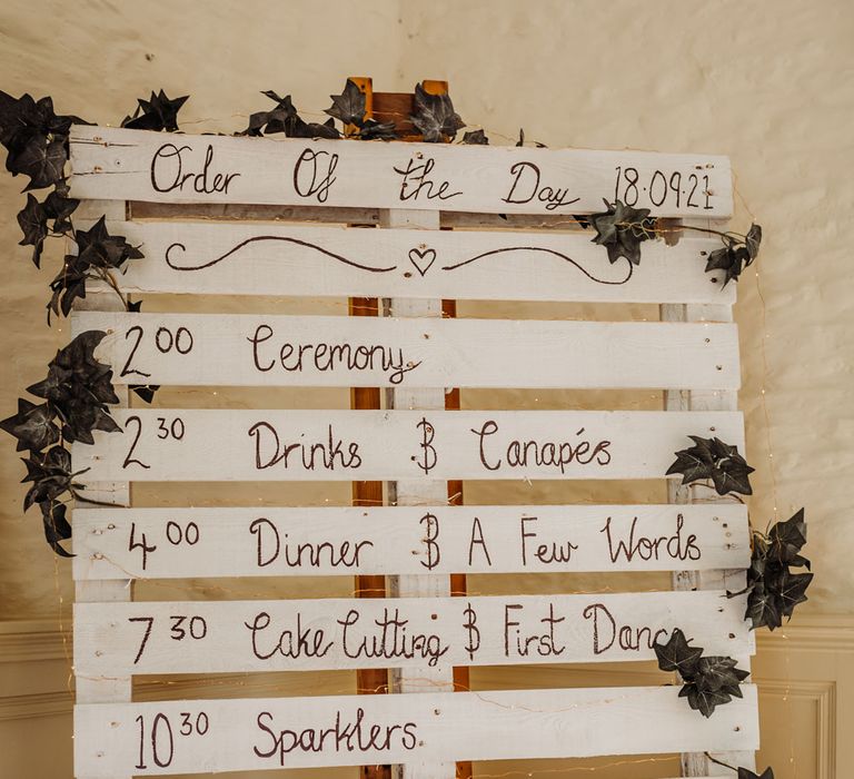 Wooden pallet wedding order of the day sign painted white with ivy garland for rustic wedding