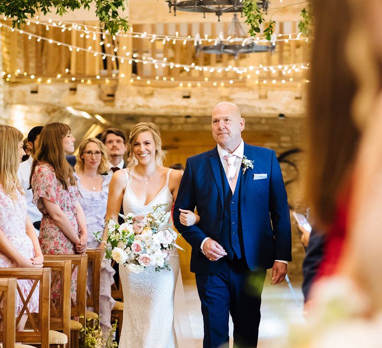 Father of the bride in a navy suit and pink tie walking his daughter down the aisle in a beaded Made With Love Bridal gown 