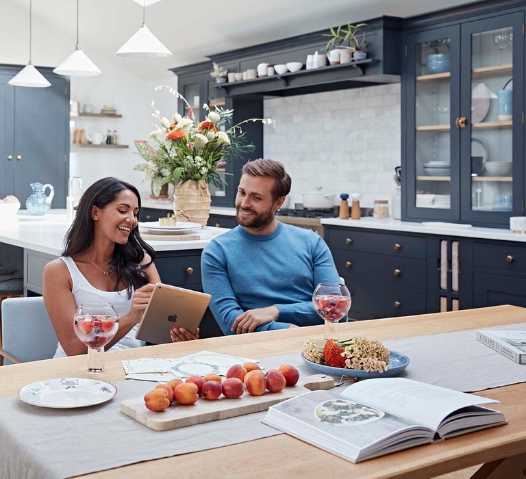 Couple sitting in their grey shaker kitchen with an iPad looking at their The Wedding Shop gift list