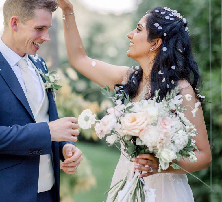 Bride & groom laugh whilst covered in confetti outdoors on their wedding day