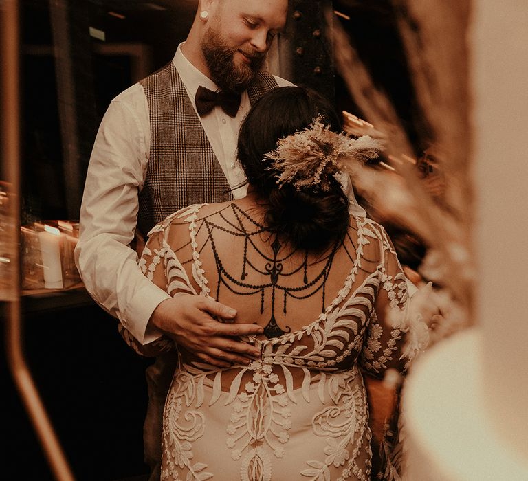 Indian bride in a lace Rue de Seine wedding dress with henna pattern on her back, pinned dup do and dried flower hair accessory 