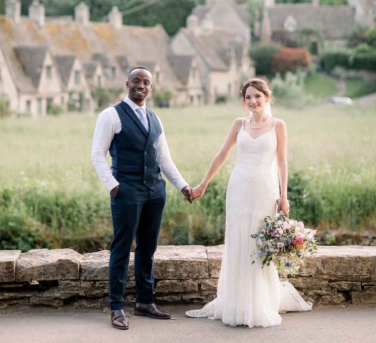 Bride & groom stand hand in hand in the Cotswolds 