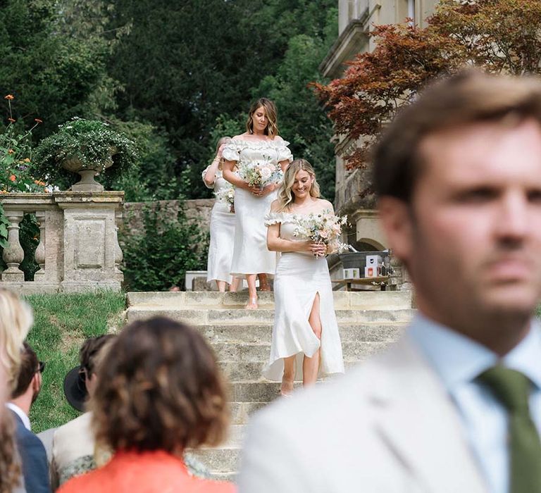 Bridesmaids approach the aisle in their white off the shoulder Bardot style dresses