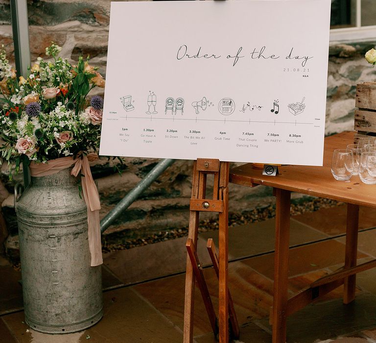 Order of the day wedding sign on dark wooden easel complete with mini pictures relating to the occasion 