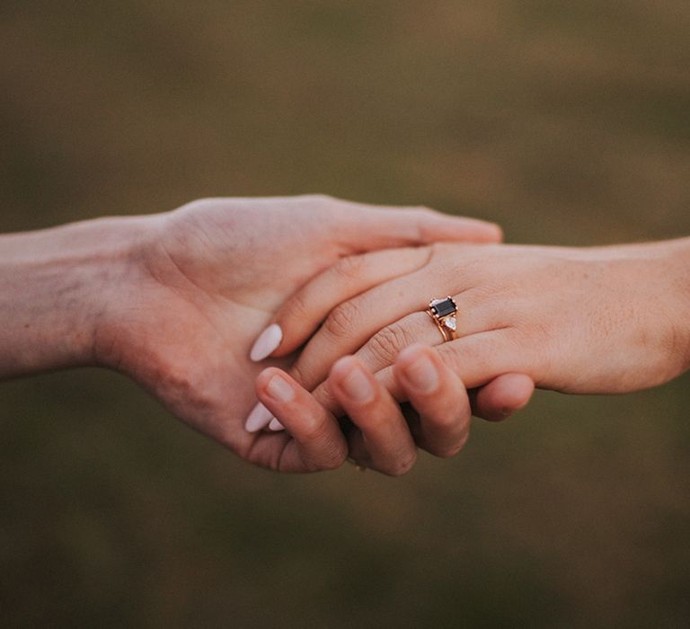 Brides hold hands with baby pink nails and dark stone engagement ring