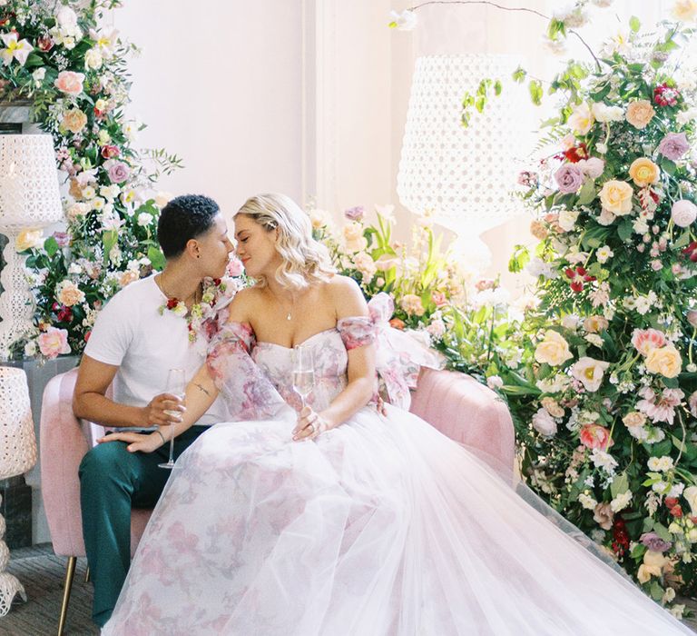 LGBTQI+ couple sitting on a pink velvet chair at Barnett Hill Hotel surrounded by floral arrangements 