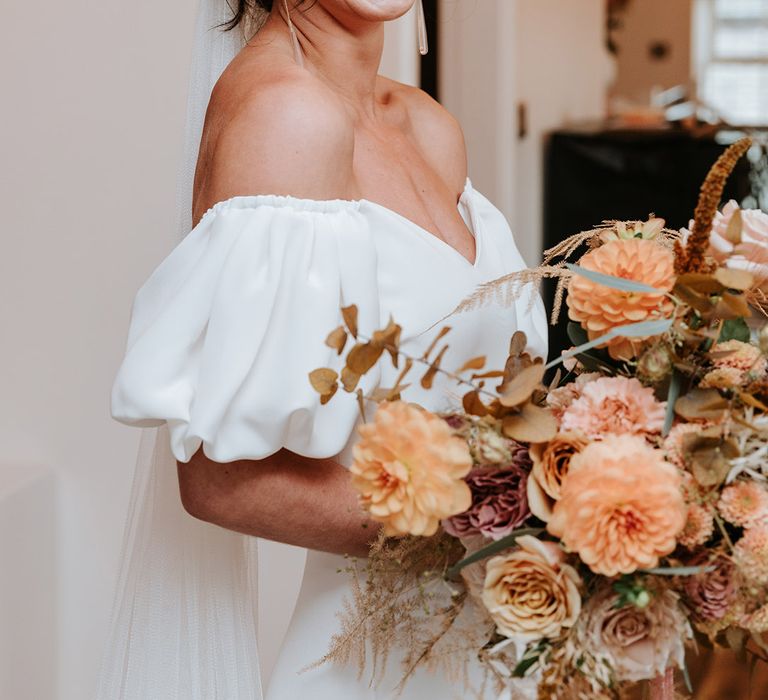 Bride in puff sleeve Alexandra Grecco dress with neutrala utumnal wedding bouquet and dangly earrings