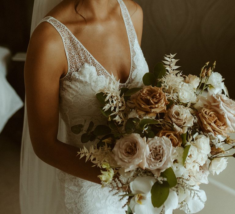 Bride in lace v-neck wedding dress with updo hairstyle and dangly earrings holding large rose bouquet