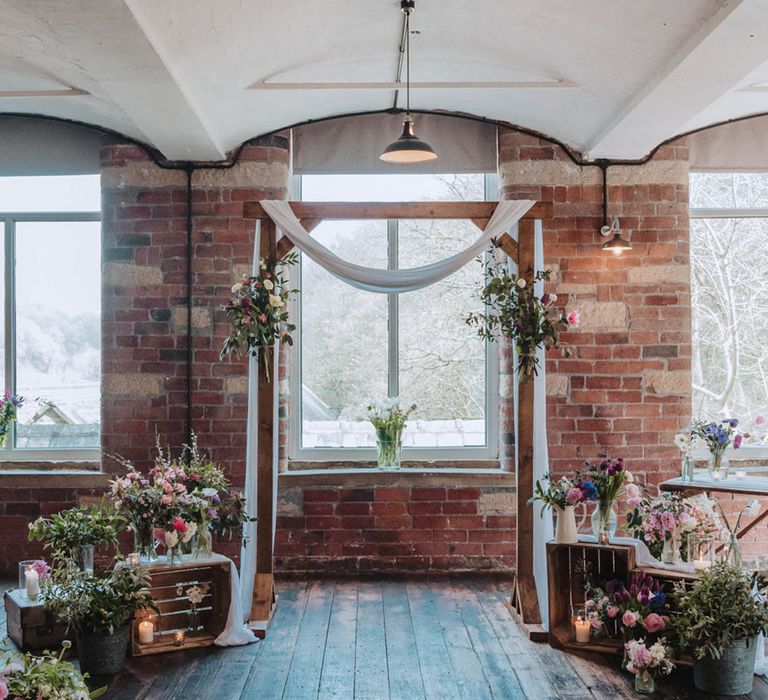 Bowers Mill industrial venue with wooden frame and drapes and pink, purple and blue flowers and wildflowers for spring wedding 