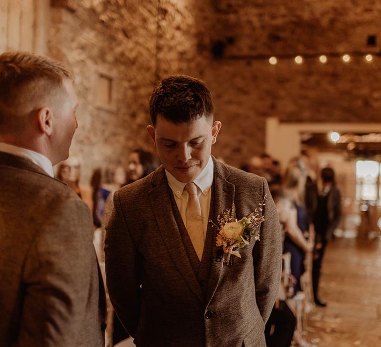 Groom in three piece brown suit waits at the altar for the bride to walk down with best man next to him 