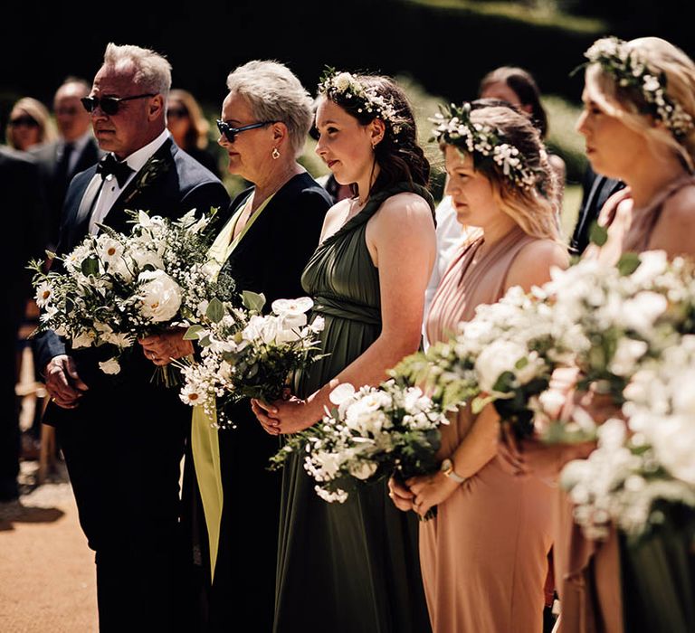 Bridesmaids in pale pink and olive green bridesmaid dresses with white flower crowns and white flower bouquets