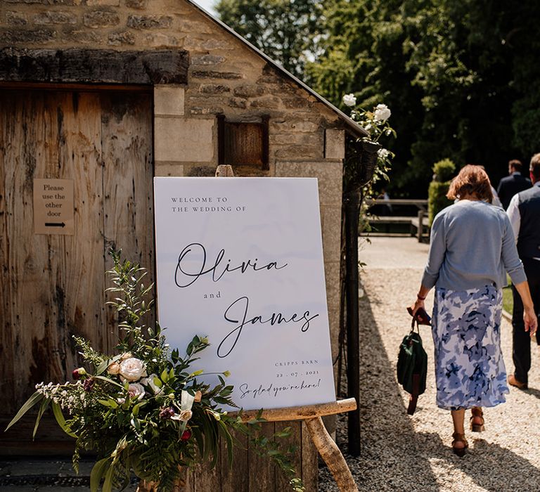 Black and white wedding welcome sign on wooden easel with white flower arrangement 