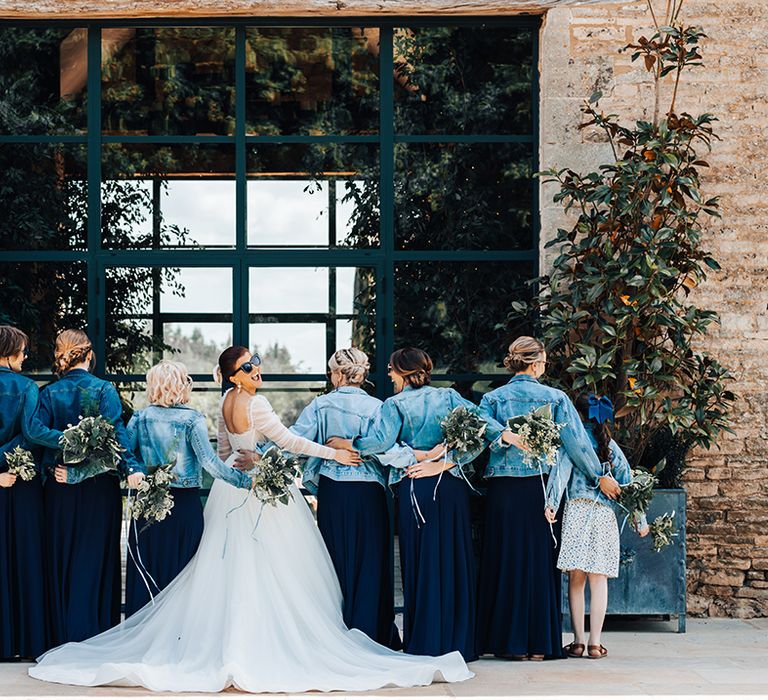 Bride looks back at the camera with sunglasses on as she poses with her bridesmaids in navy dresses with denim jackets 