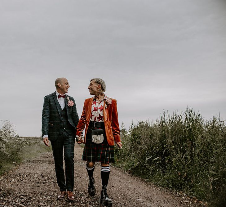 Grooms stand in the road wearing tartan suit and kilt complete with orange blazer and red bow tie 