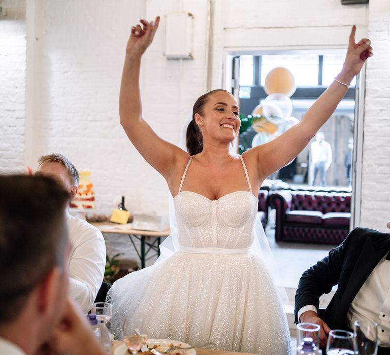 Bride dances during wedding reception as her groom wearing bright dried floral buttonhole looks on