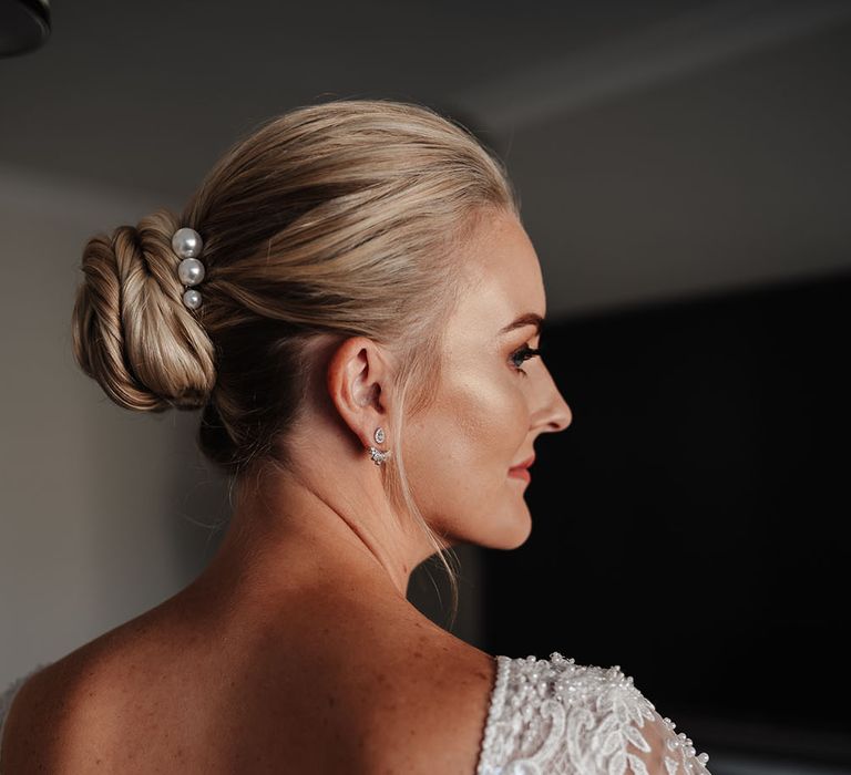 Bride wears her blonde hair in high bun complete with pearl hair accessories 