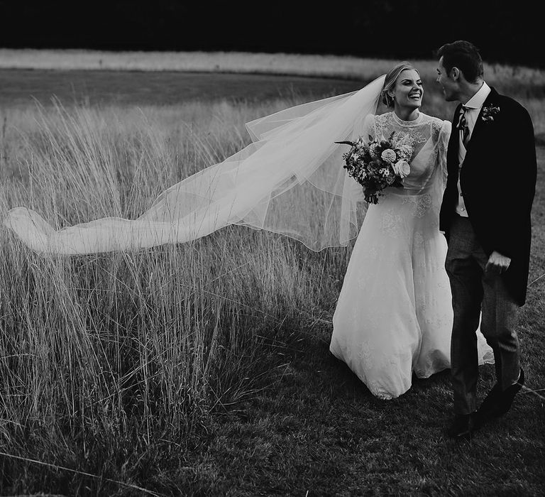 Bride's veil blows in the breeze as they stare into each other's eyes and laugh on their wedding day 