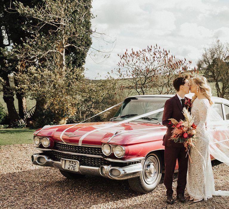 The happy couple share a kiss in front of their pink Cadillac wedding car 