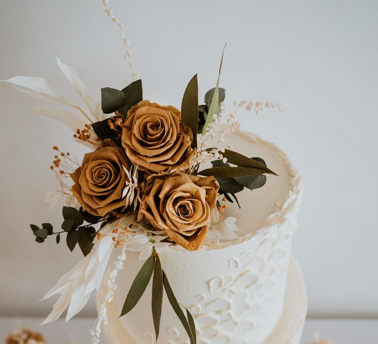 Three tiered white buttercream wedding cake with burnt orange rose decoration on top