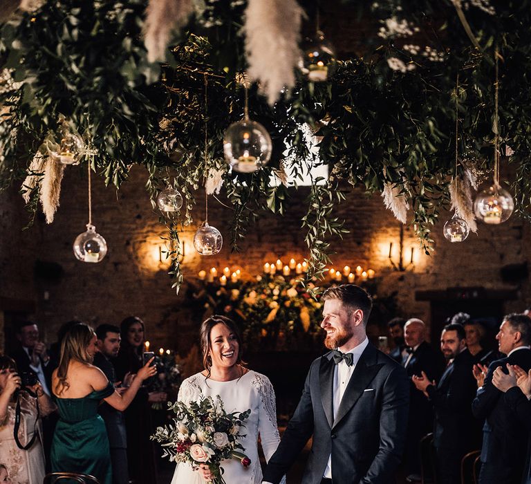 Bride and groom walk back down the aisle as a married couple with pretty winter wedding decor 