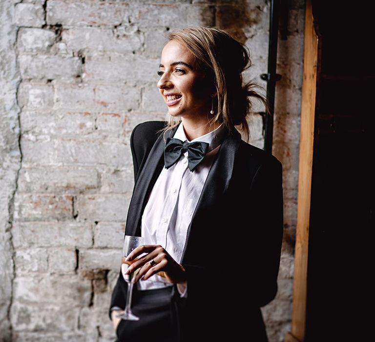 Bridesmaid in black-tie suit holds champagne glass 