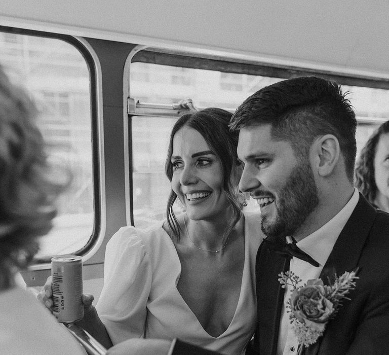 Bride in v neck wedding dress and groom in large boutonniere smiling and laughing at wedding