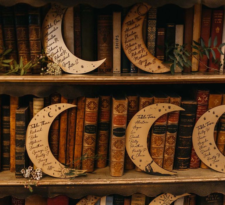 Moon shaped wooden table numbers on bookshelf surrounded by old, vintage books and foliage decorations