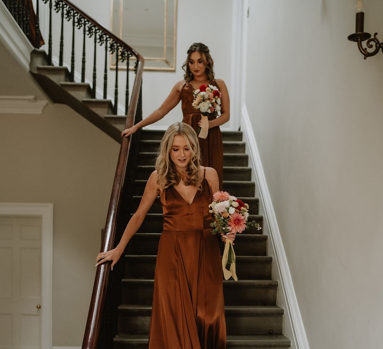 Bridesmaids in matching sleeveless v-neck burnt orange satin bridesmaid dresses holding colourful floral bouquets with yellow ribbon