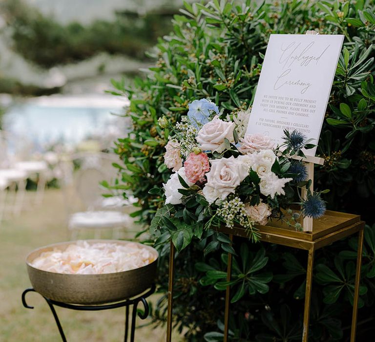 Unplugged ceremony sign on a gold table surrounded by pink roses, thistles and a bowl full of petal confetti