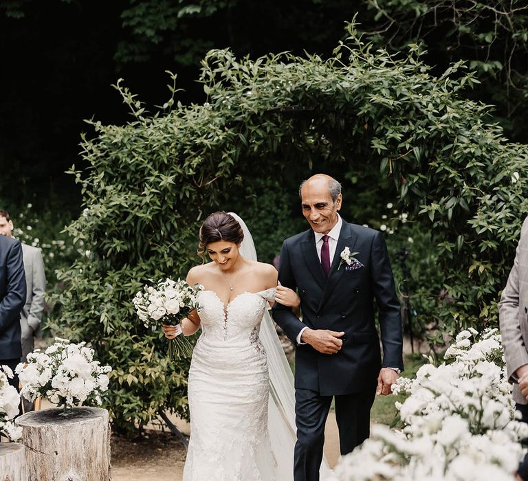 Father of the bride in black double breasted jacket with dark purple tie walking the bride down the aisle in a floral lace wedding dress 