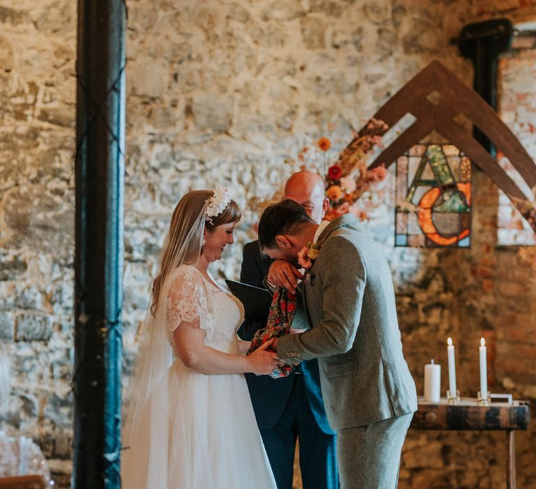 Groom in a grey wedding suit wiping his tears as he participates in the humanist and handfasting ceremony with the bride 