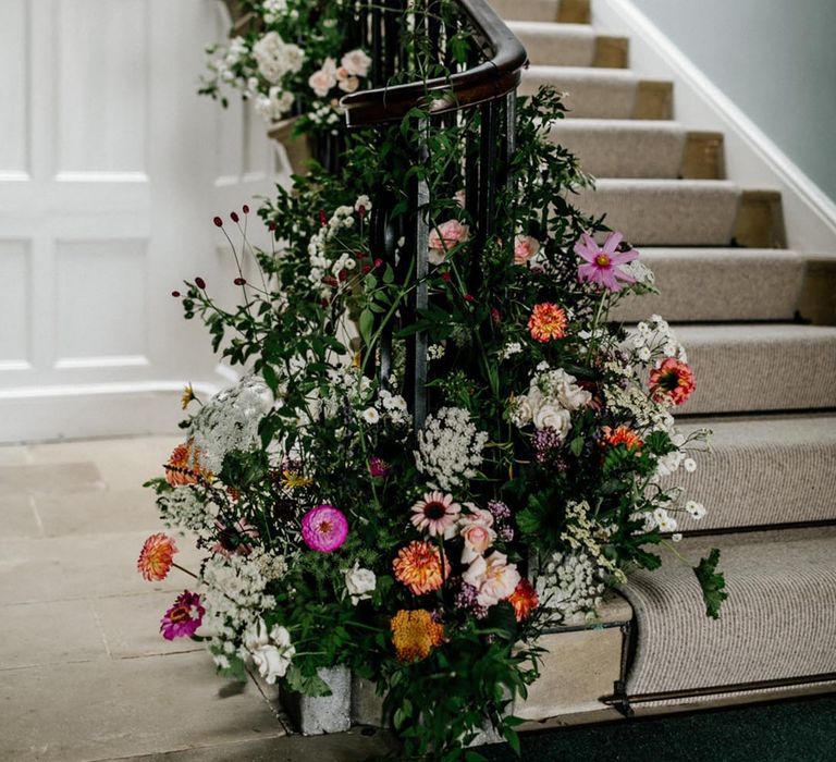 Pink, orange. and white wedding flowers with dahlias and roses with foliage decorating the bannister 