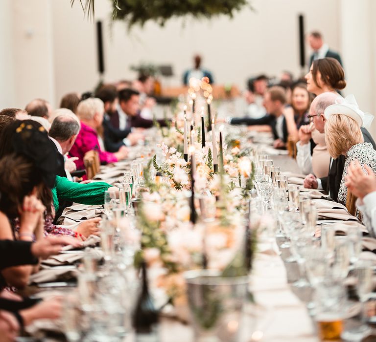 Wedding guests at The Orangery reception room chatting underneath large suspended foliage decor and festoon chandeliers 