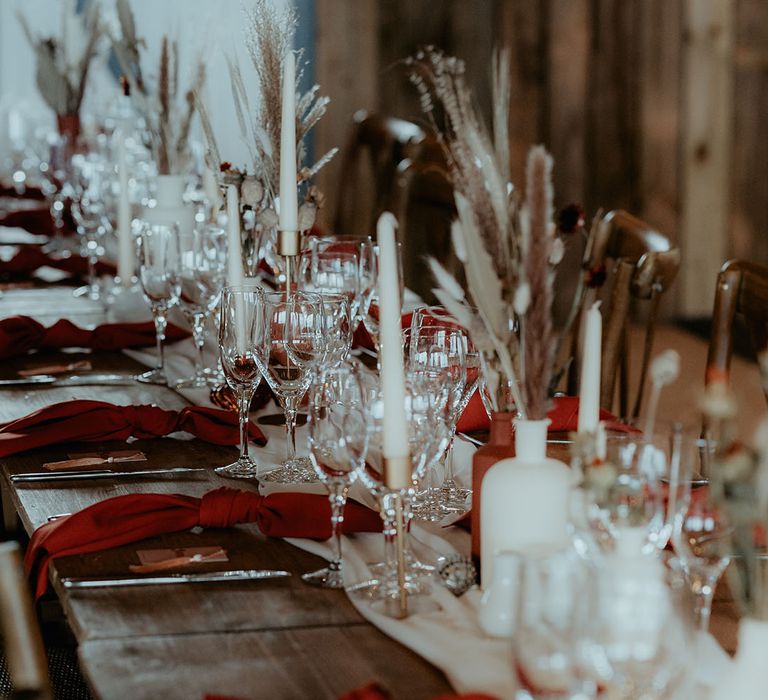 Wooden banquet table with white table runner and white candles with burnt orange napkins and bunny grass decor 