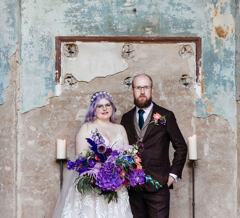 Bride in flowing leaf appliqué sheer Evie Young bridal gown and cathedral length veil standing with groom in textured mocha brown three piece groom suit with deep green tie and rose boutonniere 