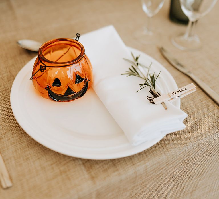 Pumpkin wedding favour on white plate with white napkin and sprig of rosemary as a place name for autumnal rustic luxe wedding 