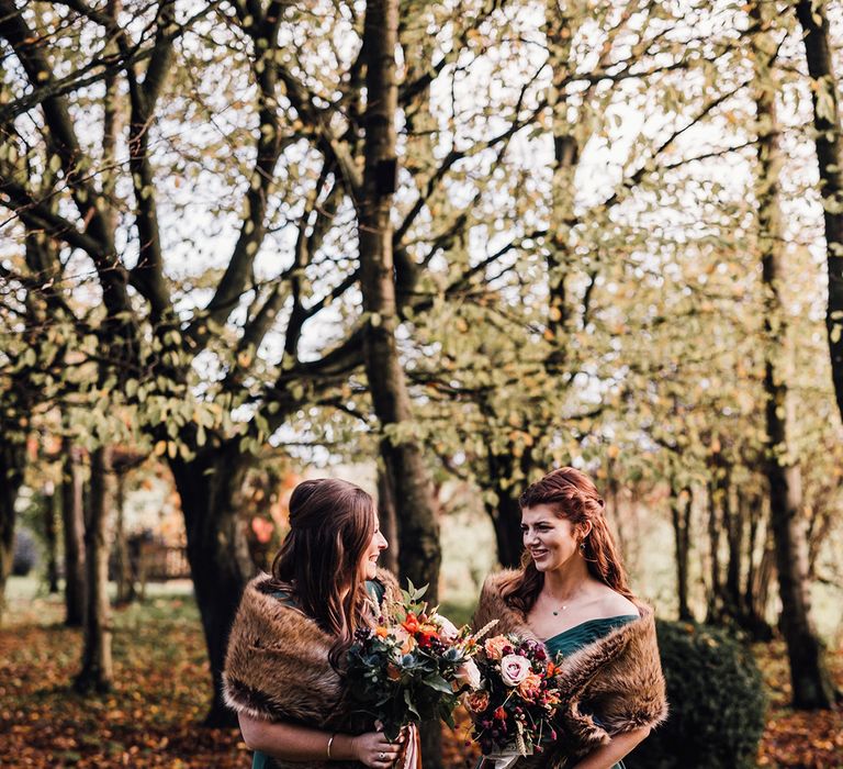 Autumnal bridesmaid dresses worn by the bridesmaids in a forest green shade with brown faux fur shawls and autumnal wedding bouquets 