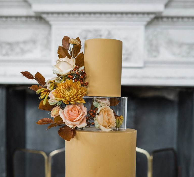 Two tier warm yellow iced wedding cake with floating layer decorated with pink ribbon and seasonal wedding flowers 