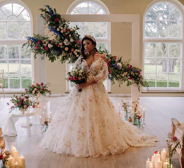 Bride in v-neck long sleeve shoulder cut out 3d appliqué wedding dress with flecks of gold wearing satin bridal headband holding large dried flower, eucalyptus, spring florals and garden rose bridal bouquet by suspended spring floral decorations and pillar candles at Braxted Park wedding venue 