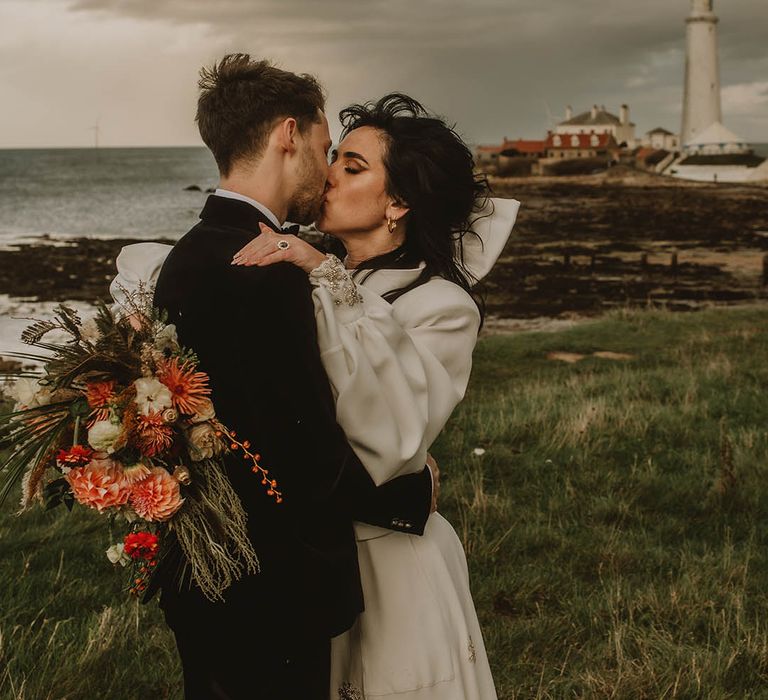 Bride in Bowen Dryden jumpsuit with large white hair bow accessory with the groom in black velvet suit 