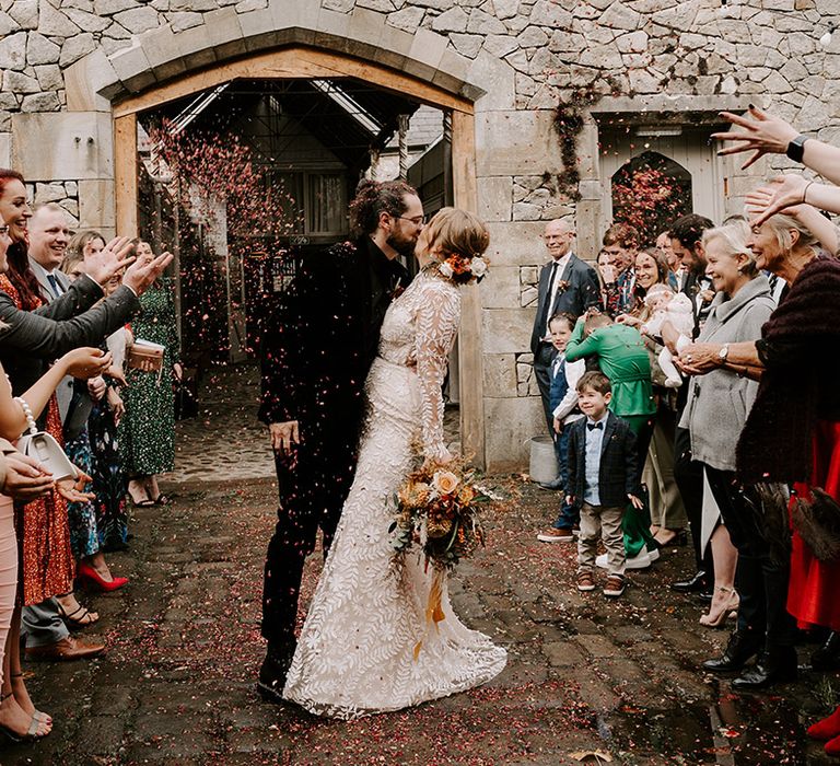 The bride and groom walk out together to the wedding guests throwing confetti 